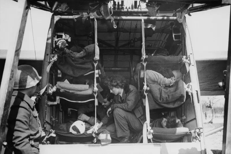 در حال خم شدن بین ردیف‌های تخت‌های سه‌طبقه، یک پرستار از واحد تخلیه هوایی ۸۱۶، به سربازان مجروح که در حال تخلیه از رود راین در آلمان، ۲۹ مارس ۱۹۴۵، می‌پرداخت، می‌پردازد (عکس AP)