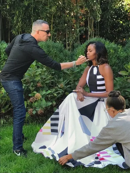 خانم اوباما، در یک گاؤن سفید با الگوهای موج‌دار پوشیده، در یک باغ نشسته است؛ آقای ری، با جین و پیراهن مشکی، در حال آرایش با رژ لب است. زنی دامن بلند را صاف می‌کند.