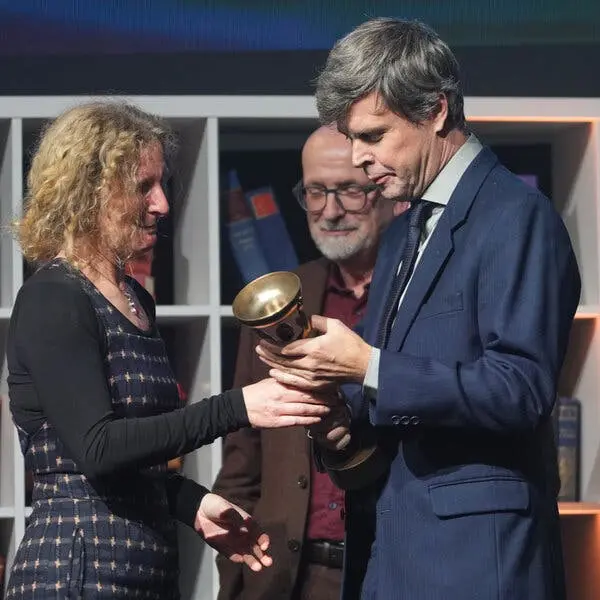 مردی در کت و شلوار که یک جایزه را از یک زن میپذیرد.