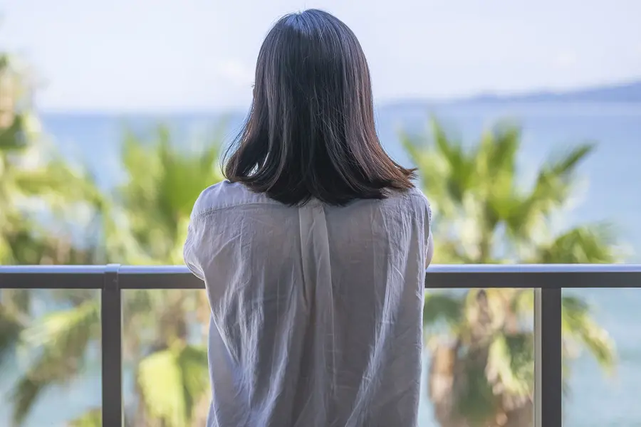 زن در تعطیلات در کنار دریا، در حال استراحت و نگاه به دریا از بالکن، در فوکوکا، ژاپن - عکس استوک