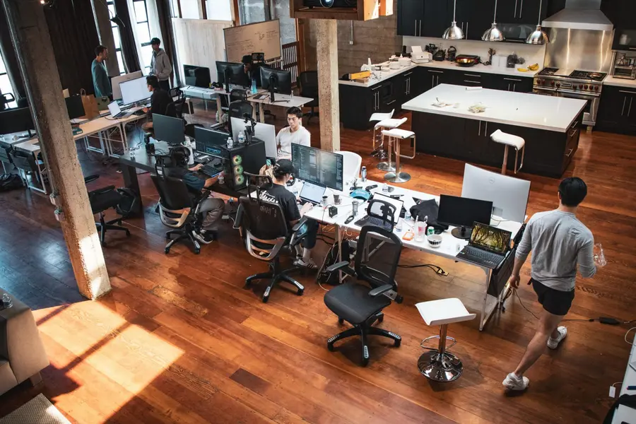 فضای کاری باز شامل افرادی است که در میزهای کاری با چندین کامپیوتر کار می‌کنند، یک ناحیهٔ آشپزخانه در پشت، و کف‌پوش چوبی در تمام فضا.