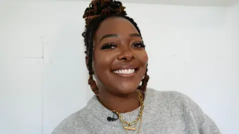 جان فیراهال/بی‌بی‌سی: شئا اوسی به دوربین لبخند می‌زند؛ موهایش سیاه و حلقه‌ای هستند، در بینی‌اش حلقه‌ای دارد و سوئیتری خاکستری به تن دارد و جلوی دیوار سفیدی ایستاده است