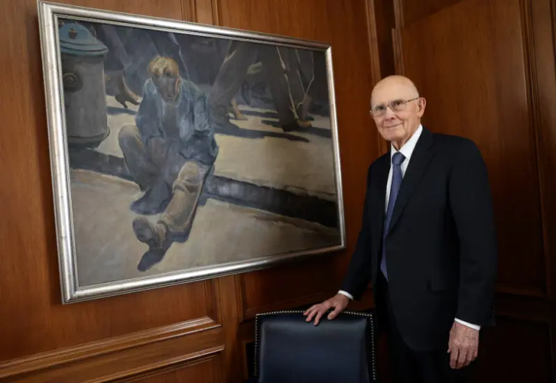 رئیس دالین اچ. اوکس در کنار نقاشی «مرد فراموش‌شده» در دفترش