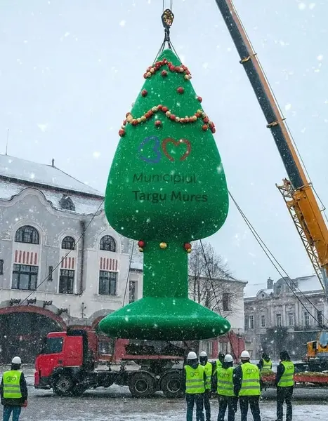 کارگران تزئین بزرگ سبز به شکل درخت را با جرثقیل در میدانی برفی هدایت میکنند