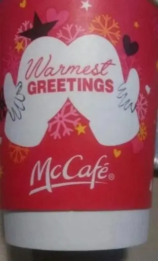 یک فنجان قرمز McCafé با متن «گرمترین تبریکها»، تزئینشده با دانههای برف، قلبها و گرافیک دستکشهای نوکدست