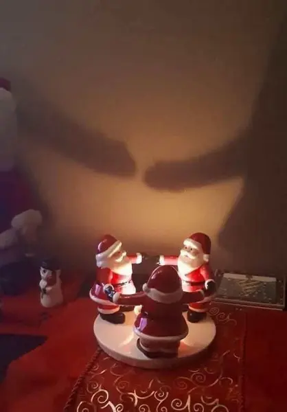 سه فیگور سانتا در یک دایره قرار گرفتهاند که سایهای وهمآور شبیه چهره بر دیوار میاندازند؛ یک آدمبرفی در نزدیکی آن دیده میشود
