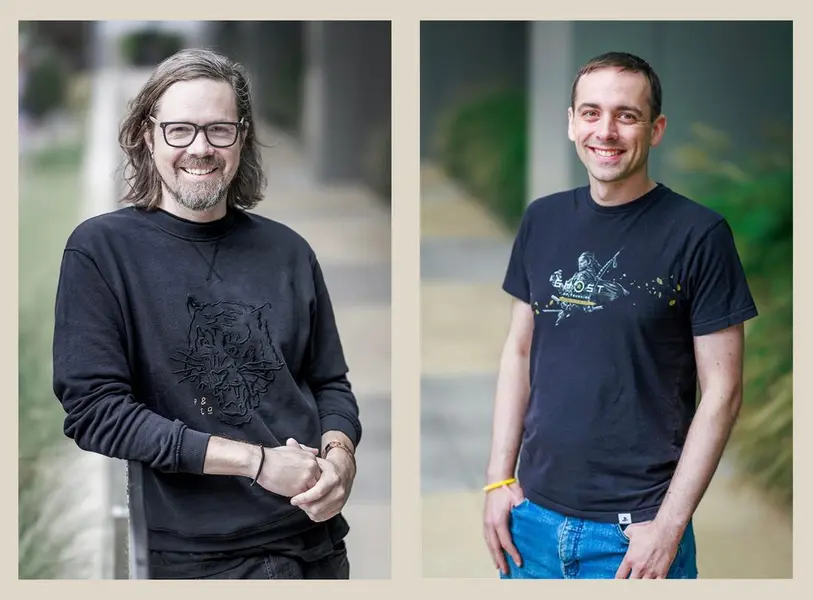 جیسن کنل در سمت چپ با پیراهن آستین بلند خاکستری، ایدریان بنتلی در سمت راست با تی‌شرت آبی تیره. پس‌زمینه شامل سبزی‌های محو