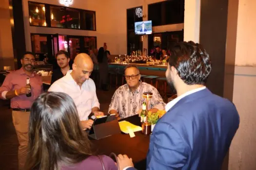 شبکهسازان در یک بار فورت لاودرادل برای یک رویداد میزبانی شده توسط گروهی در جنوب فلوریدا به نام Sunset Connect گرد هم آمدند. نیاز رو به رشد به فضاهای سوم که با اضطراب اقتصادی همراه است، تقاضا برای برنامهها و گروههایی که حرفهای و شخصی را ترکیب میکنند، افزوده است. (Esther Deutsch/Courtesy)