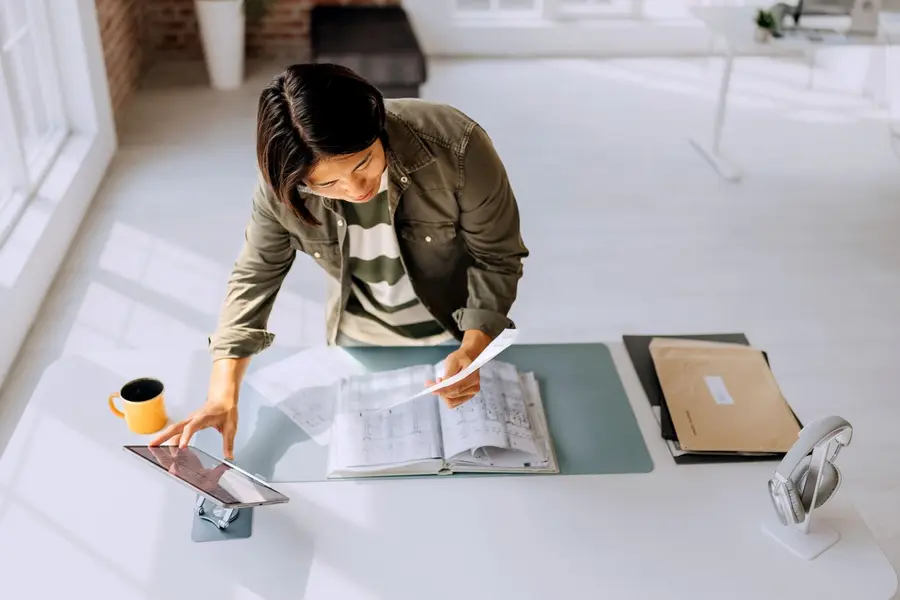 معمار با لباس غیررسمی که در یک دفتر مدرن و مینیمالیستی طرحی را بررسی میکند